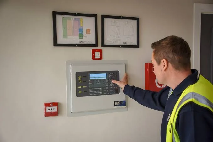 An engineer testing a fire alarm control panel next to a zone plan