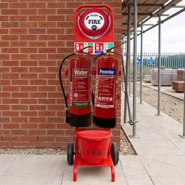 A fire point with water and powder extinguishers on a wheeled stand beside a manual call point